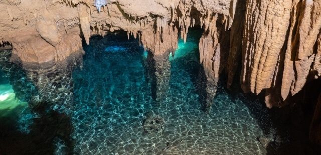 Clear blue water beneath stalactites in a submerged limestone cave